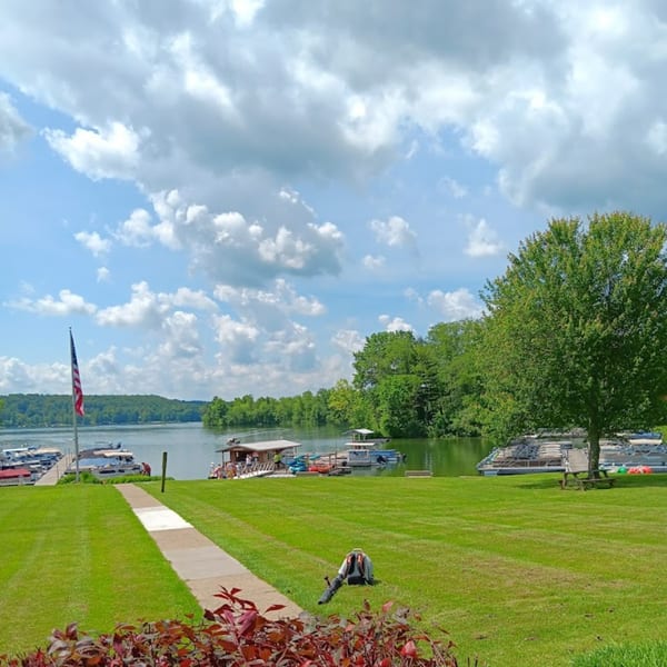 Lighthouse Bistro's lakeside view with a lush green lawn, boats docked, and a distant wooded shoreline.